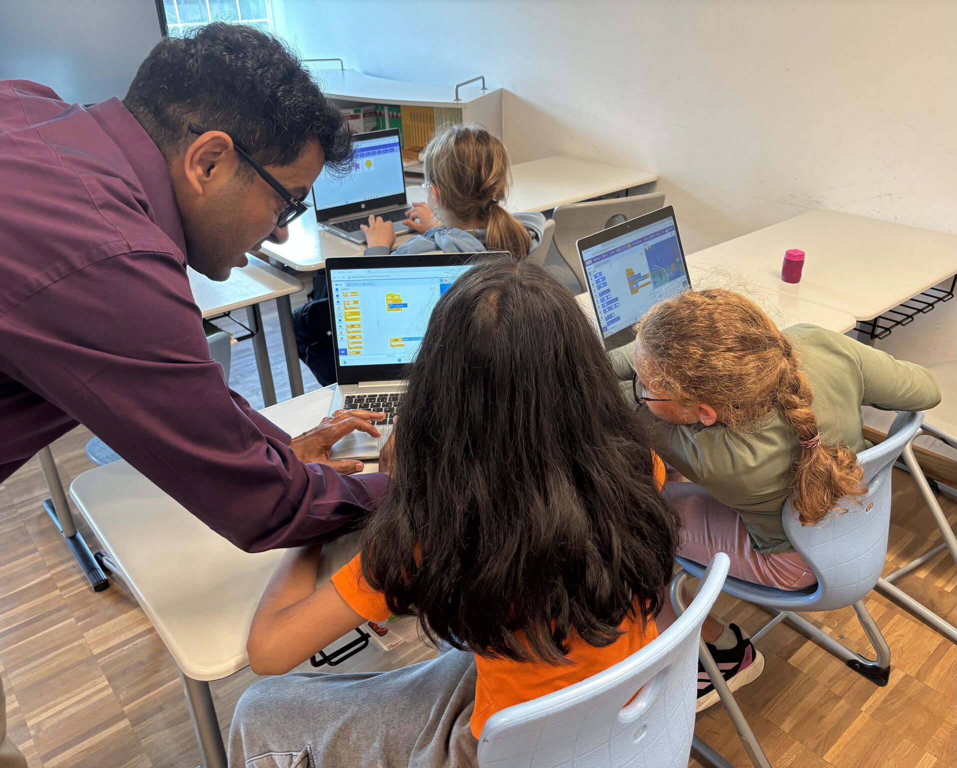 Coach hilft drei jungen Menschen, auf ihrem Laptop mit Scratch zu programmieren